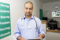 Портрет впевненого лікаря-чоловіка з цифровим планшетом в лікарняному коридорі — стокове фото
