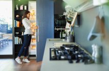 Женщина, стоящая у открытого холодильника на кухне — стоковое фото