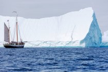 Barco navegando cerca de majestuoso iceberg soleado en el Océano Atlántico Groenlandia - foto de stock