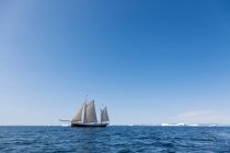 Barco navegando más allá del derretimiento del hielo polar en el soleado océano Atlántico azul Groenlandia - foto de stock