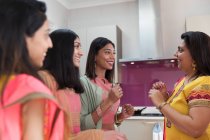 Mulheres indianas felizes em saris falando na cozinha — Fotografia de Stock