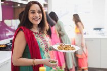 Portrait happy Indian woman in sari eating in kitchen — Stock Photo