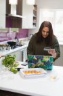 Женщина с кредитной картой покупки онлайн на ноутбуке на кухне — стоковое фото