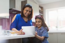 Mãe e filha felizes usando tablet digital na cozinha — Fotografia de Stock