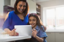 Mãe e filha felizes usando tablet digital na cozinha — Fotografia de Stock