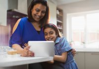 Улыбающиеся мать и дочь с помощью цифрового планшета на кухне — стоковое фото
