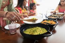 Mujeres indias en saris sirviendo y comiendo comida en la mesa - foto de stock