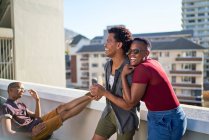 Счастливая молодая пара смеется и обнимается на солнечном городском балконе — стоковое фото