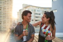 Felice giovane coppia bere birra sul balcone soleggiato sul tetto urbano — Foto stock