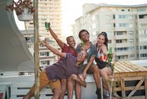 Portrait carefree young friends drinking beer on urban rooftop balcony — Stock Photo