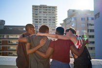 Jovens amigos abraçando na varanda ensolarada do telhado urbano — Fotografia de Stock