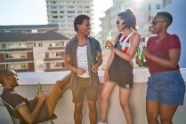 Счастливые молодые друзья пьют пиво на солнечном городском балконе на крыше — стоковое фото