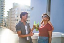 Happy young friends drinking beer on sunny urban rooftop balcony — Stock Photo