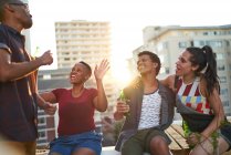 Счастливые молодые друзья пьют пиво на солнечной городской крыше — стоковое фото