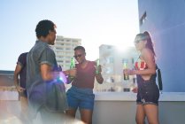 Jóvenes amigos bailando y bebiendo cerveza en el soleado balcón de la azotea urbana - foto de stock