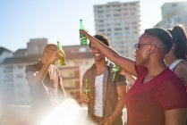 Carefree young friends drinking beer on sunny urban balcony — Stock Photo