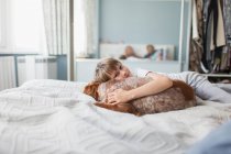 Retrato lindo chico abrazo perro en la cama - foto de stock