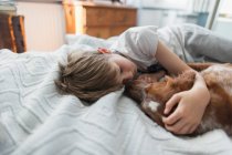 Милый мальчик обнимает собаку в постели — стоковое фото