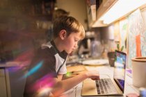 Focused boy doing homework at laptop in kitchen — Stock Photo