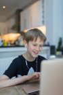 Улыбающийся мальчик с наушниками на домашнем обучении за ноутбуком — стоковое фото