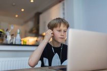 Мальчик с наушниками на домашнем обучении за ноутбуком — стоковое фото