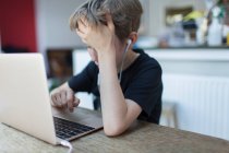 Разочарованный мальчик с наушниками на домашнем обучении за ноутбуком — стоковое фото