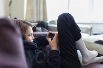 Мальчик играет в видеоигру со смартфоном на диване — стоковое фото