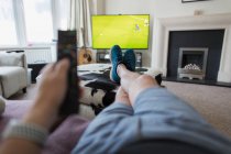 POV man on sofa with remote control watching soccer match on TV — Stock Photo