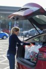 Mujer cargando comestibles en la parte trasera del coche en el estacionamiento - foto de stock