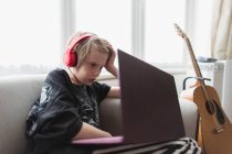 Junge mit Kopfhörer und Laptop auf Wohnzimmersofa — Stockfoto