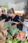 Frau und Söhne laden frische Produkte aus Kiste in Küche — Stockfoto