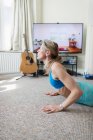 Donna che pratica yoga in TV in soggiorno — Foto stock