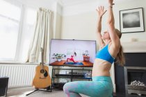 Mujer practicando yoga en la TV en el salón - foto de stock