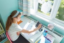 Дівчина з цифровим планшетом домашнє навчання за столом у сонячній спальні — стокове фото
