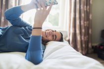 Feliz adolescente usando el teléfono inteligente en la cama - foto de stock