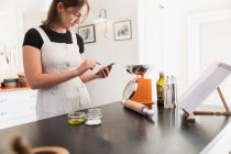 Дівчина-підліток зі смартфоном випічка на кухні — стокове фото