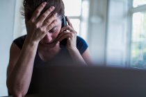 Donna frustrata che parla al telefono al computer portatile — Foto stock