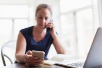 Woman talking on telephone and using smart phone at home — Stock Photo