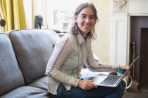 Portrait smiling teenage girl using laptop on sofa — Stock Photo