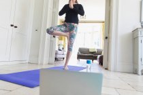 Женщина практикует йогу онлайн с ноутбуком дома — стоковое фото