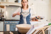 Adolescente cribado harina para hornear en la cocina - foto de stock
