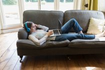 Девочка-подросток с наушниками и ноутбуком в чате на диване в гостиной — стоковое фото