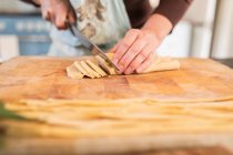 Close up woman cutting fresh homemade dough on cutting board — Stock Photo