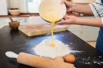 Девочка-подросток наливает яичные желтки в мучное гнездо на кухонном столе — стоковое фото