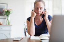 Woman working from home talking on telephone — Stock Photo