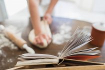 Close up woman kneading dough below cookbook — Stock Photo
