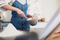 Teenage girl with whisk and bowl baking in kitchen — Stock Photo