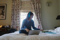 Teenage girl with headphones and laptop studying on bed — Stock Photo