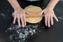Frau rollt Teig mit Nudelholz auf bemehlter Küchentheke — Stockfoto