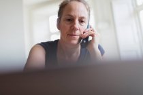Woman talking on telephone and working at laptop — Stock Photo